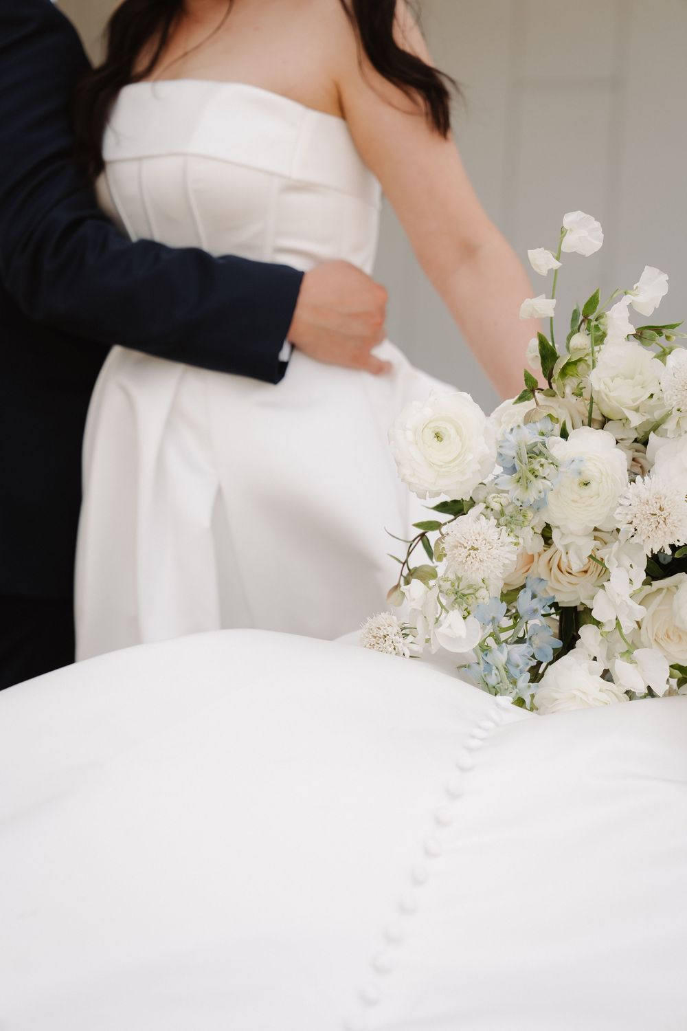 A close-up view of a white wedding dress with delicate floral arrangements featuring white blooms and greenery.