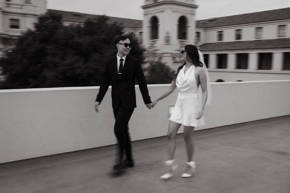 A couple walking together on a rooftop terrace, with one in a black suit and one in a white dress.