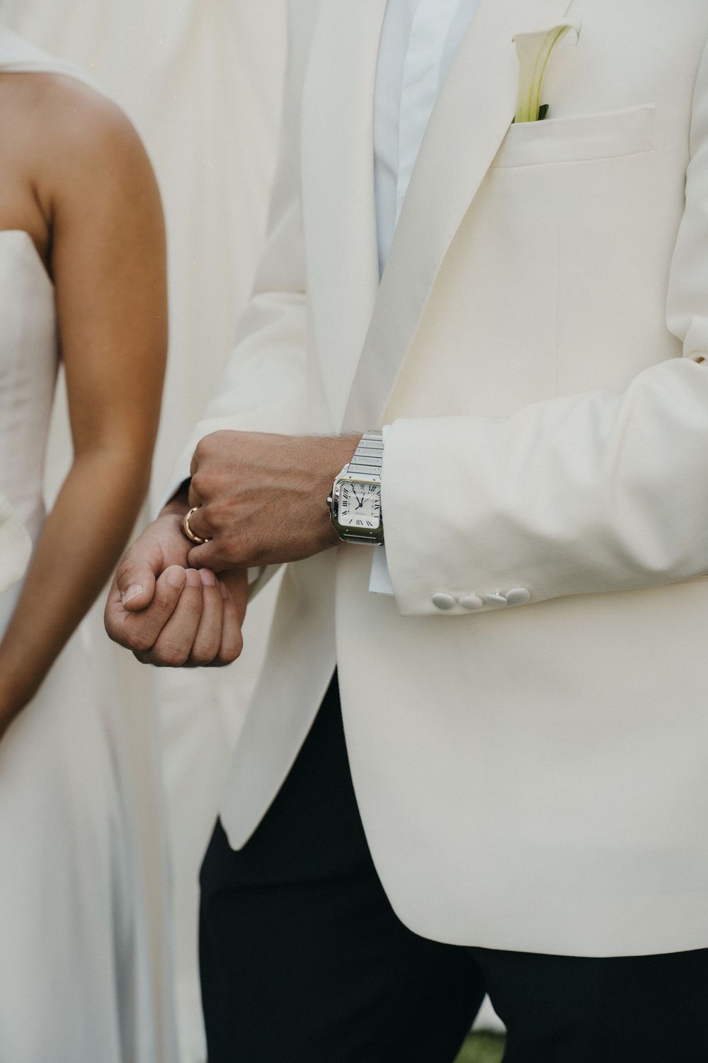 Close-up view of hands wearing formal attire showing details of white dress shirt cuffs and black pants.