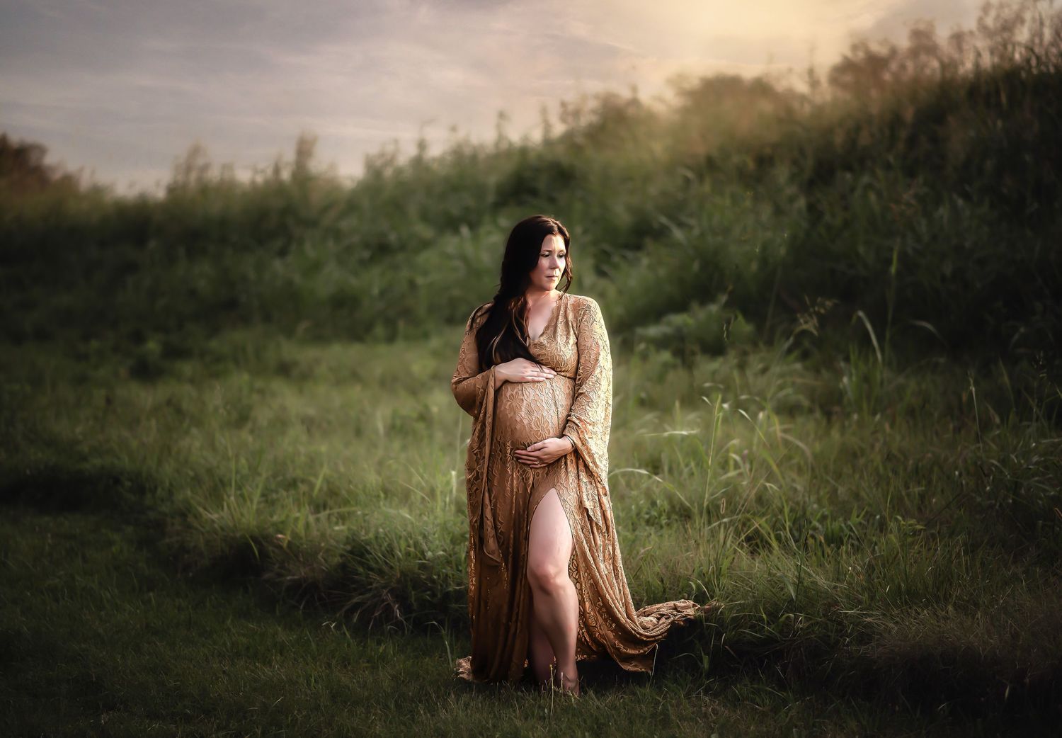 A pregnant figure in a flowing peach dress stands in a sunlit meadow during golden hour.