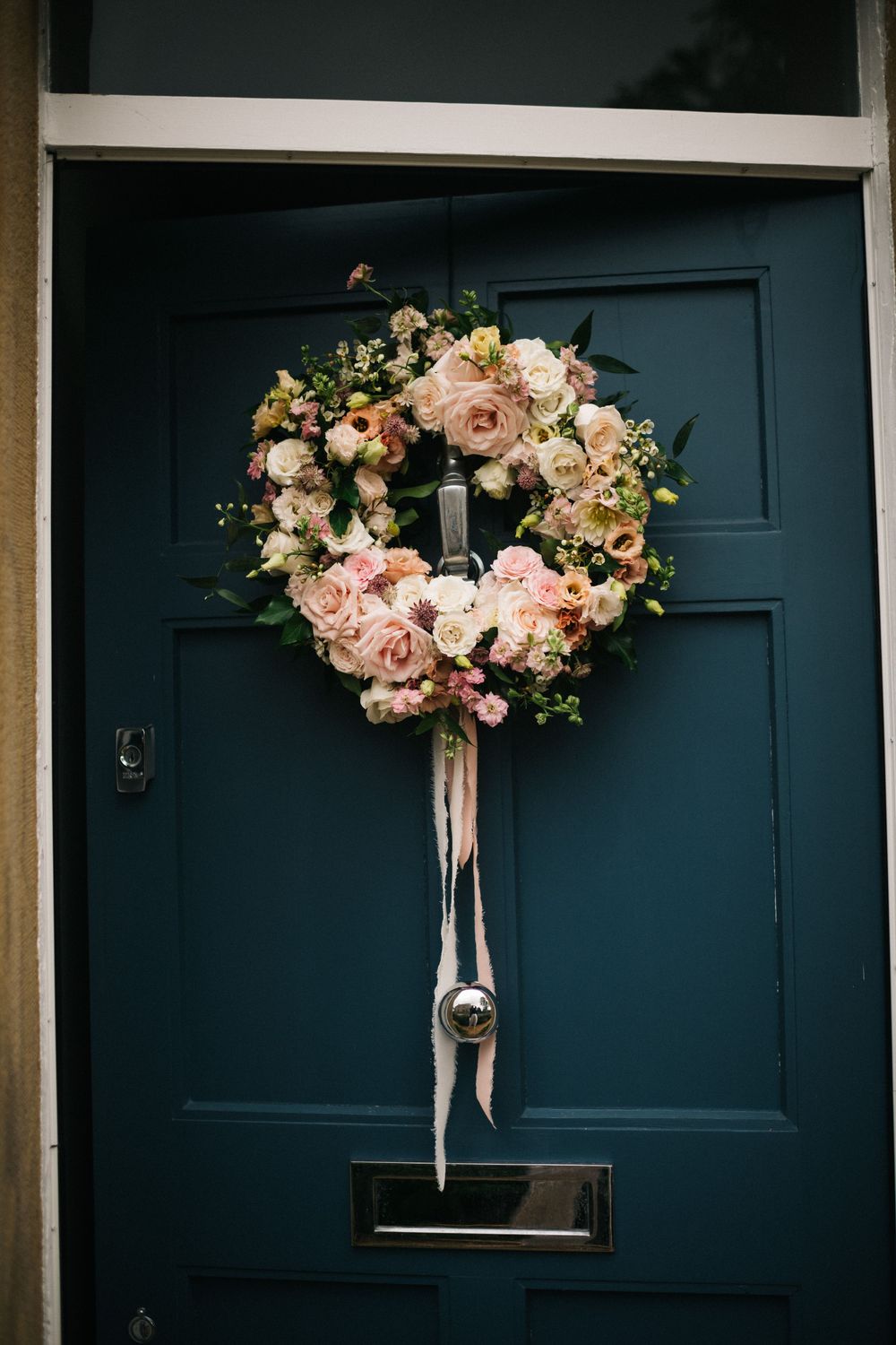 Elegant floral wreaths with pink and peach blooms adorn navy blue doors.