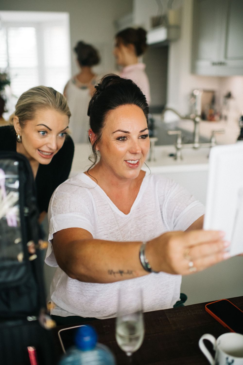 Two people laughing and having fun while taking selfies in a bright modern kitchen setting.