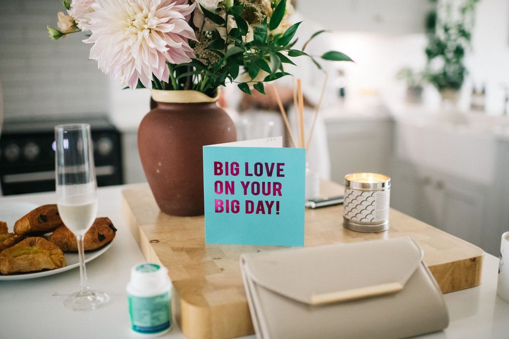 Turquoise greeting card reading 'Big Love on Your Big Day' displayed on table with pink flowers in terracotta vase.
