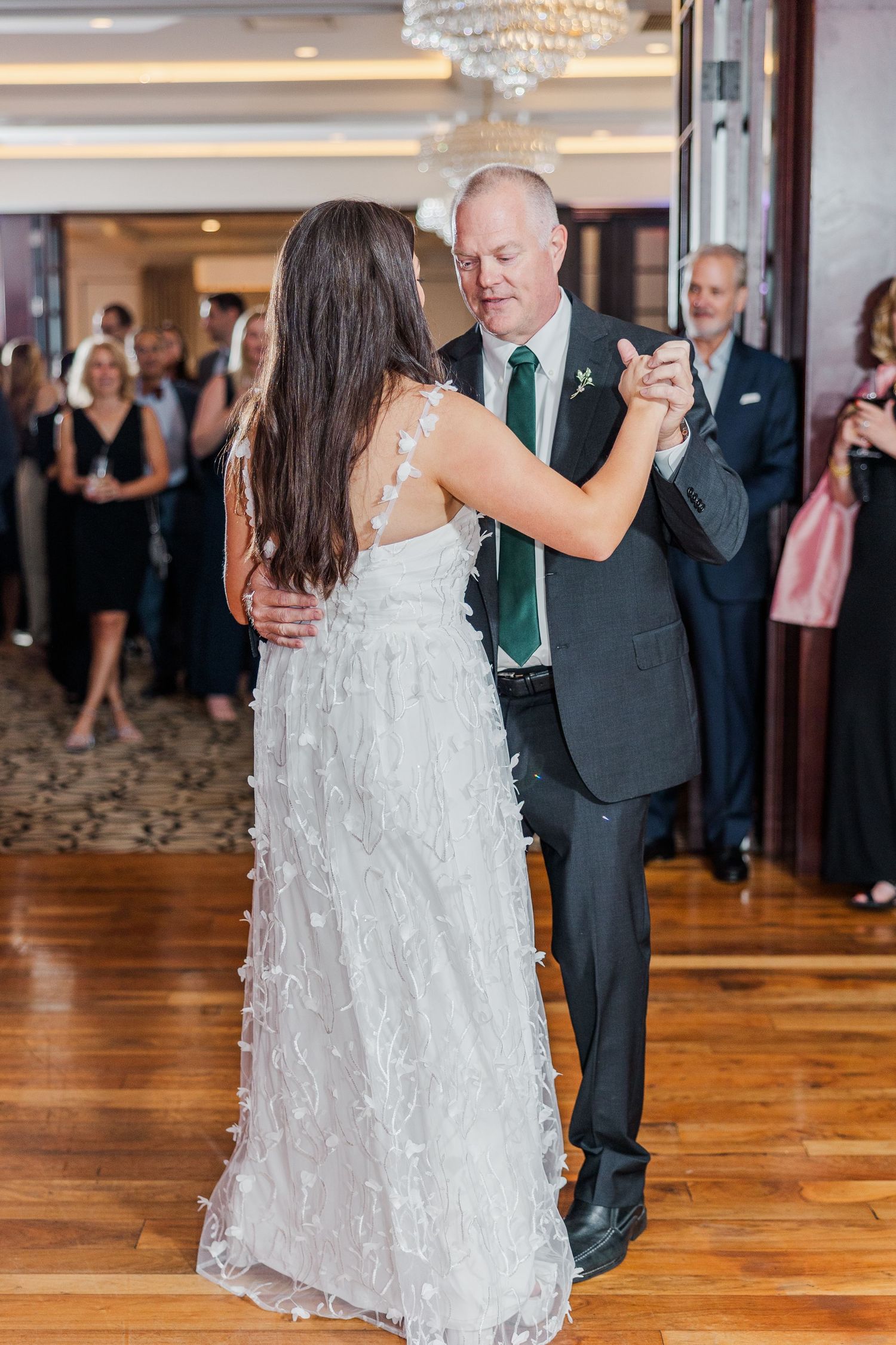 A bride in a white lace gown dances with a partner in a dark suit during a wedding reception.