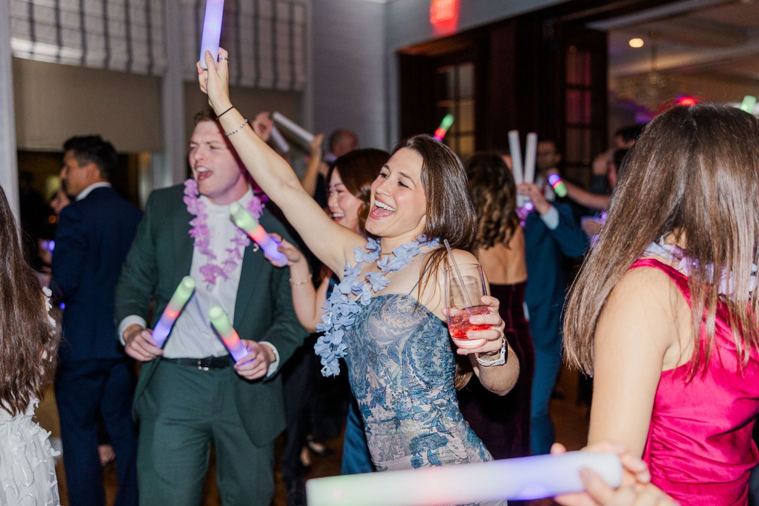 People dancing and celebrating at a lively indoor reception event with colorful lighting and formal attire.