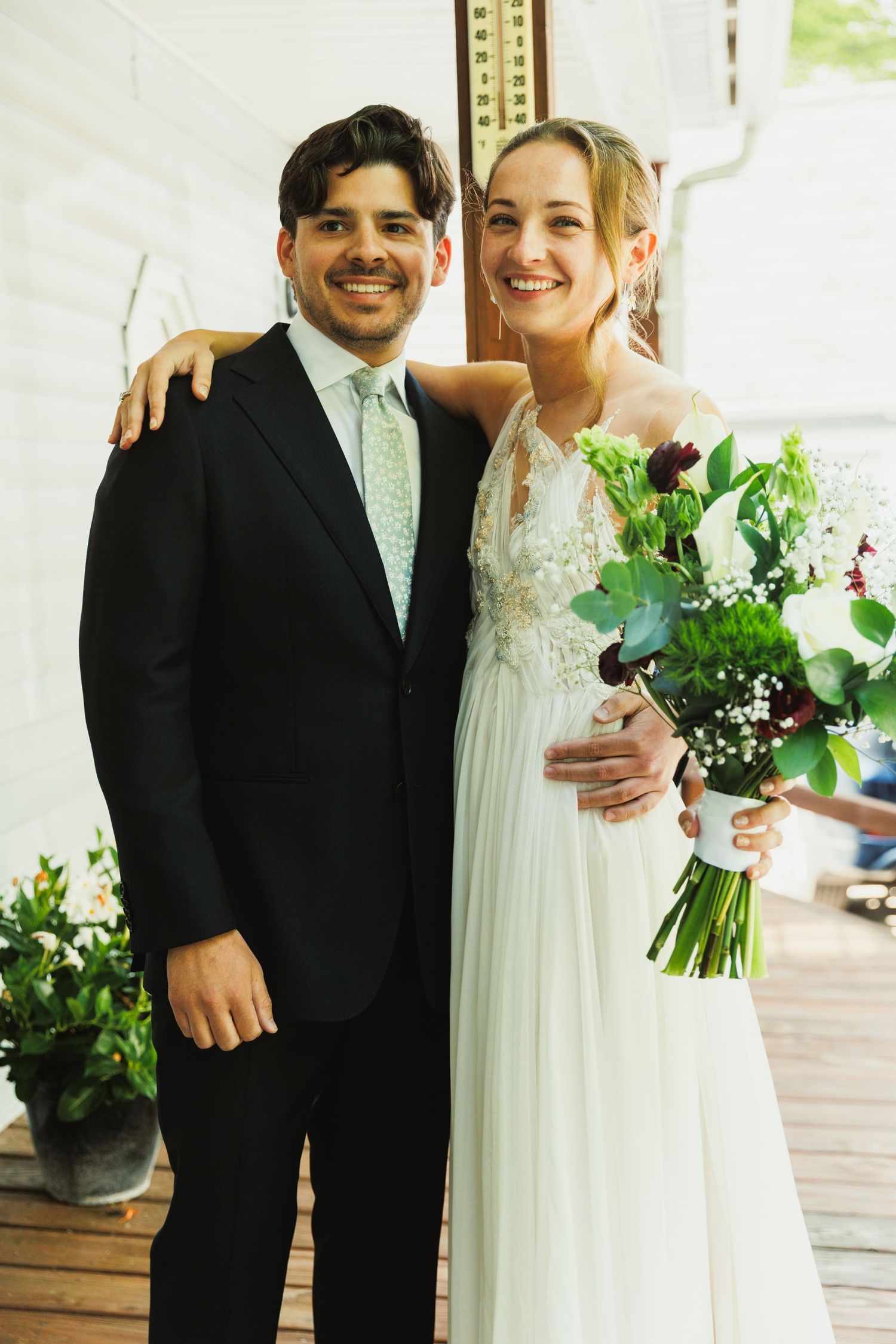 A happy couple poses together on their wedding day holding a white and green bouquet.