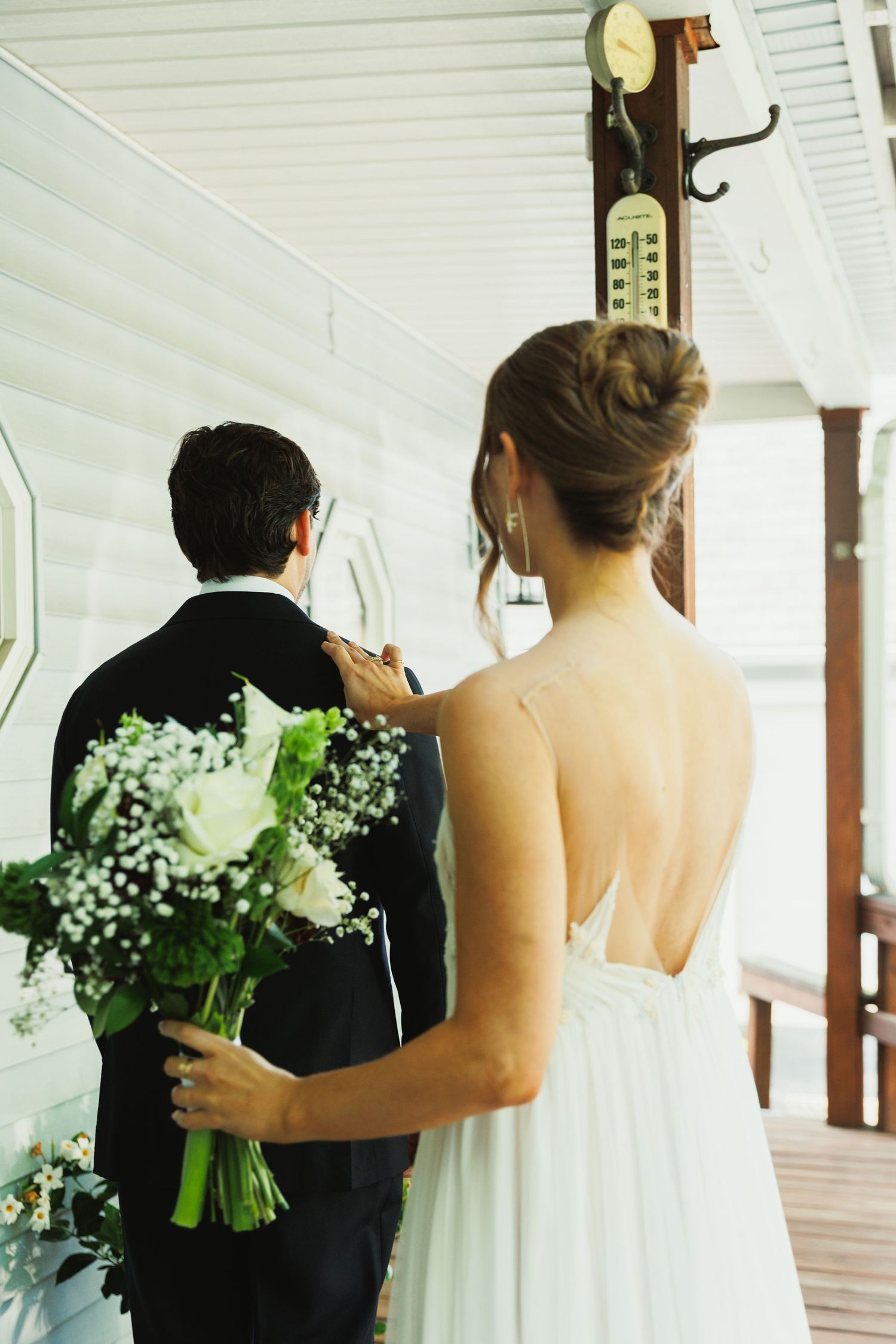 A wedding first look moment on a covered porch with white bouquets.
