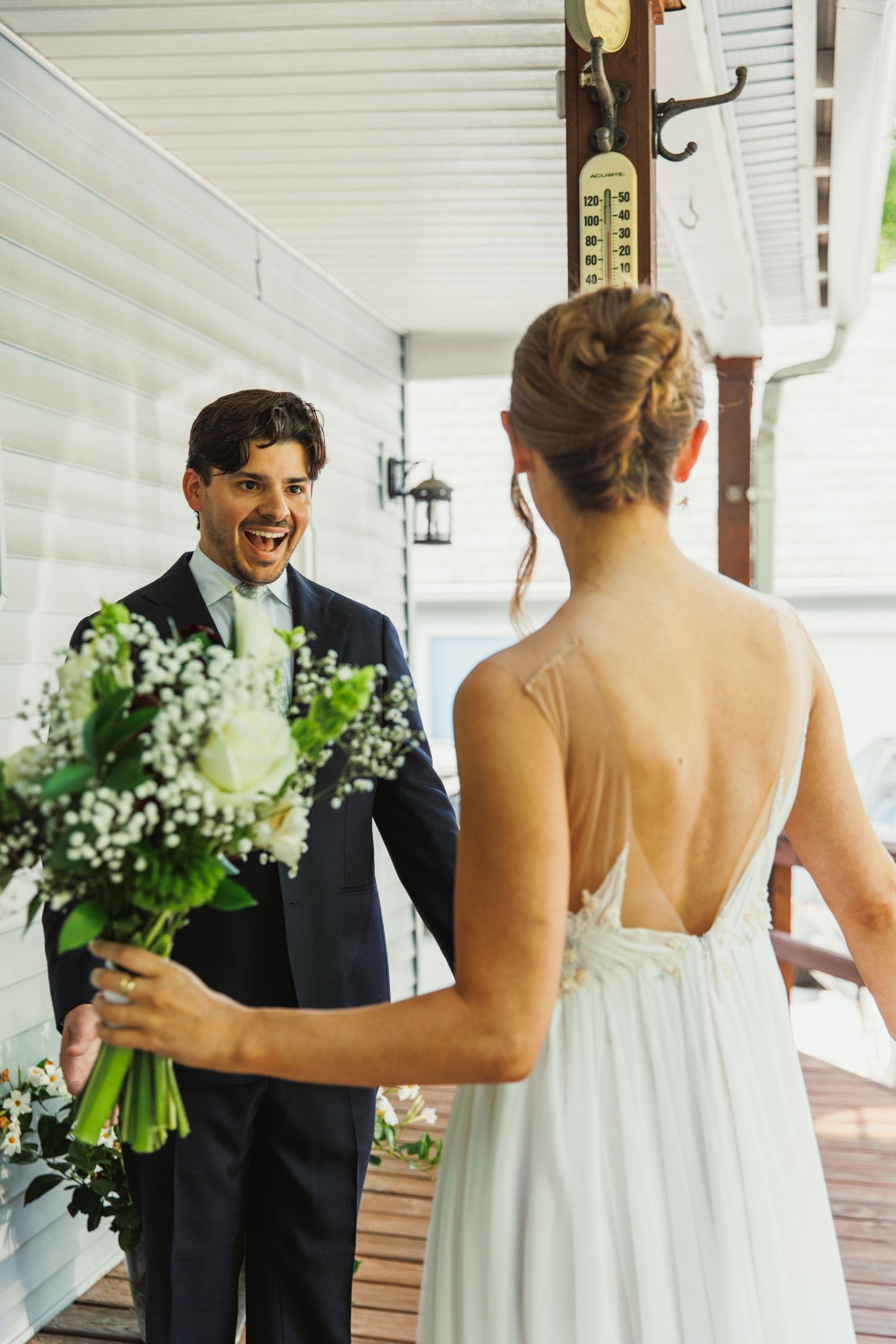 An emotional first look between a couple on a covered porch with white flowers.