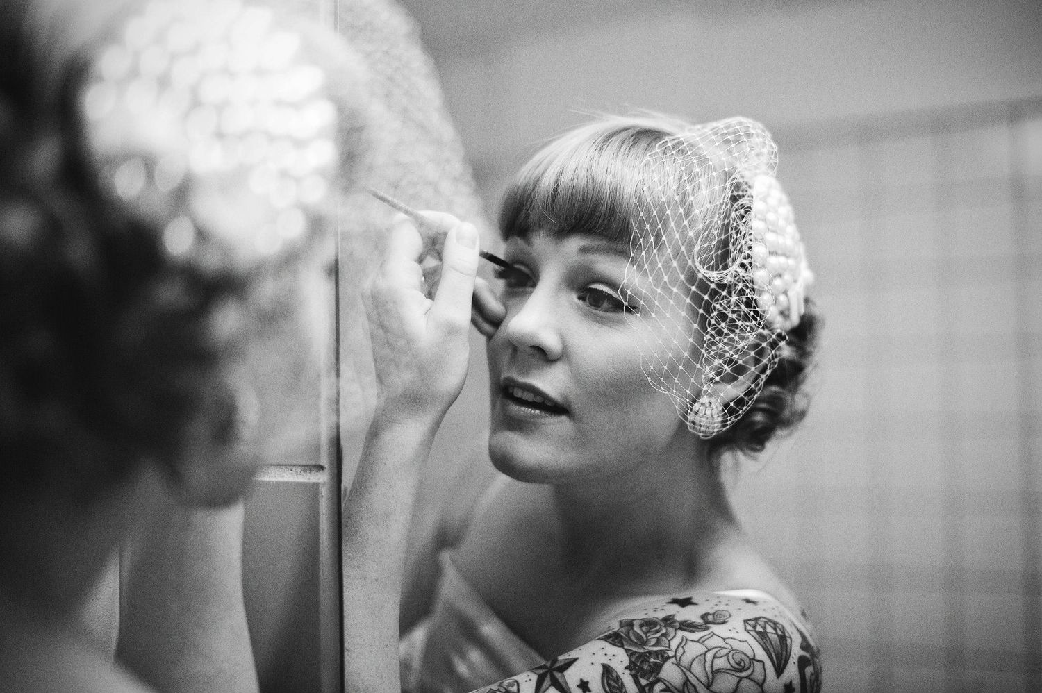 Vintage black and white photo of someone applying makeup in a mirror wearing a delicate veil.