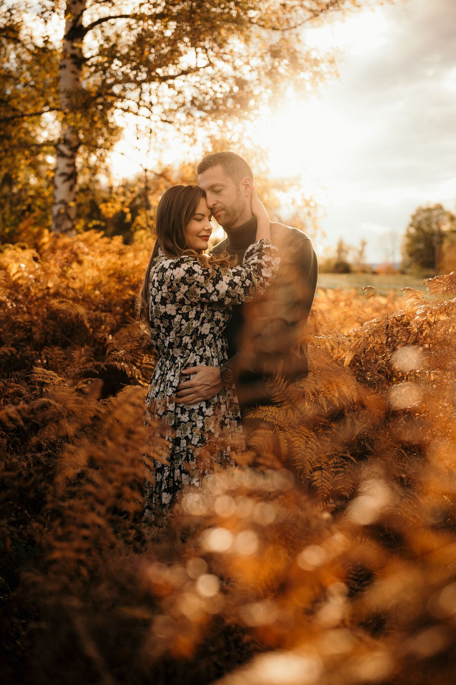 A romantic autumn portrait of a couple embracing among golden ferns at sunset.