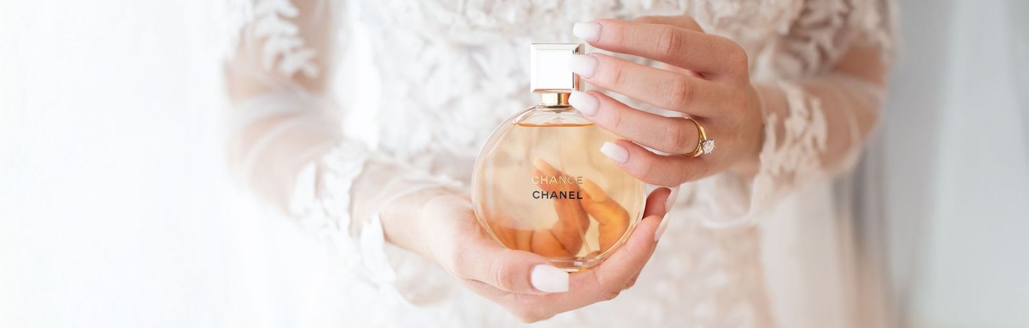 Bride in lace wedding dress holds a Chanel perfume bottle in her elegantly manicured hands.