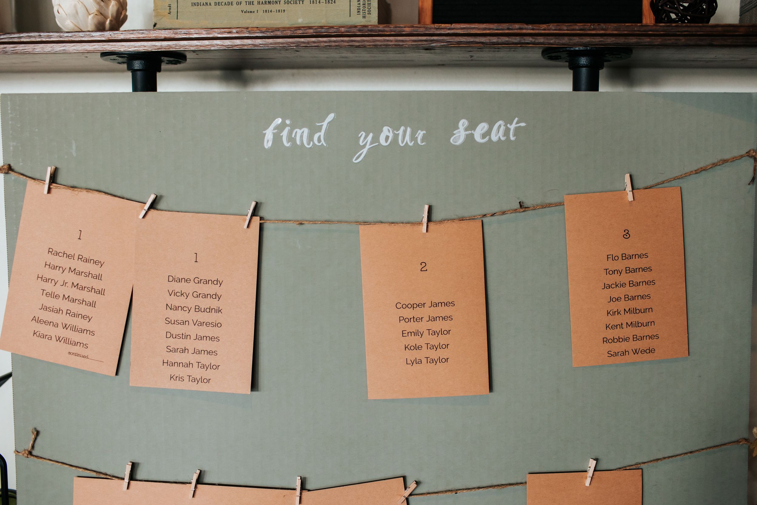 Orange paper cards hang from twine lines against a sage green wall in what appears to be a creative display setup.