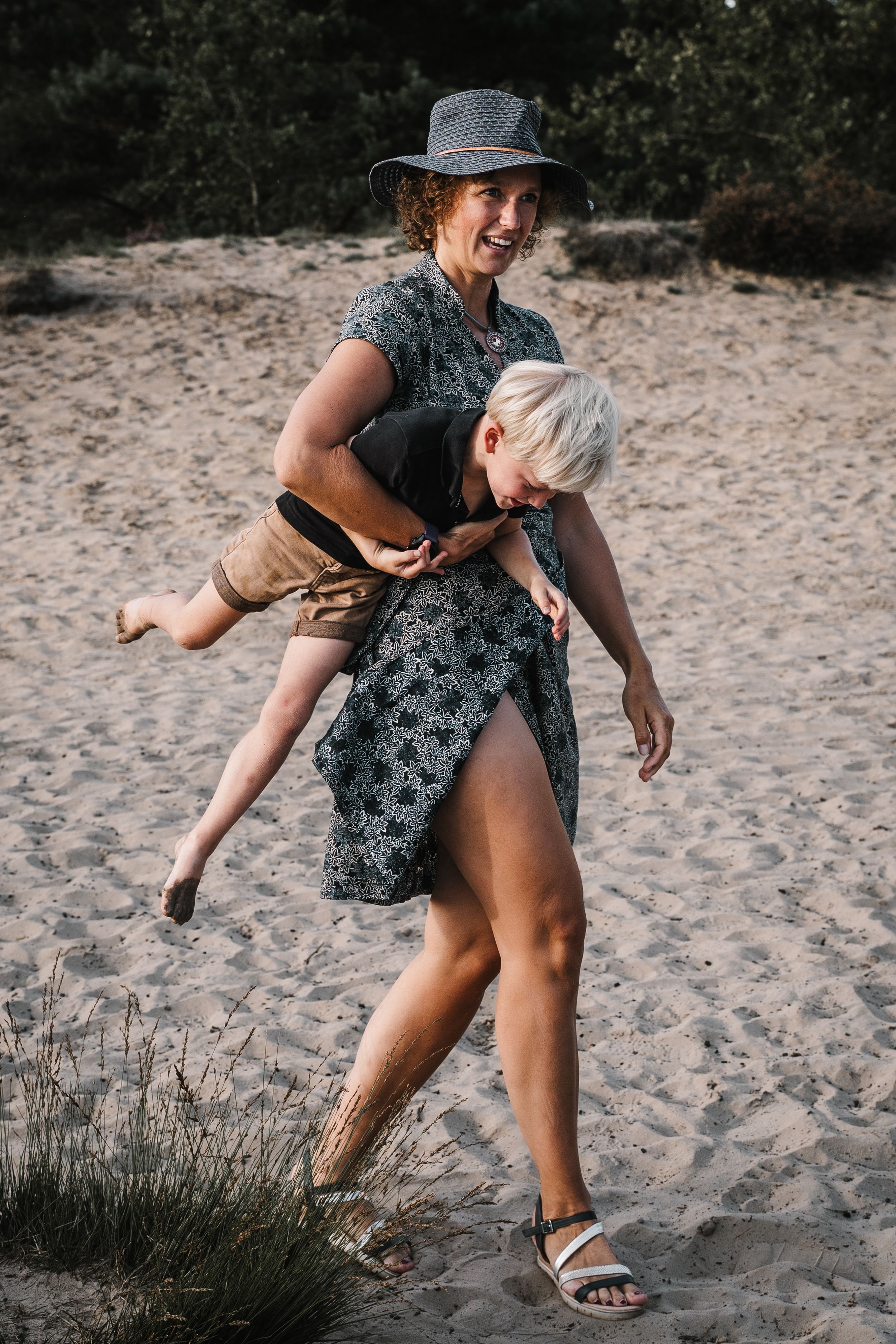Person wearing a floral dress and hat bends down to pick something up from sandy beach in sequence of action shots.