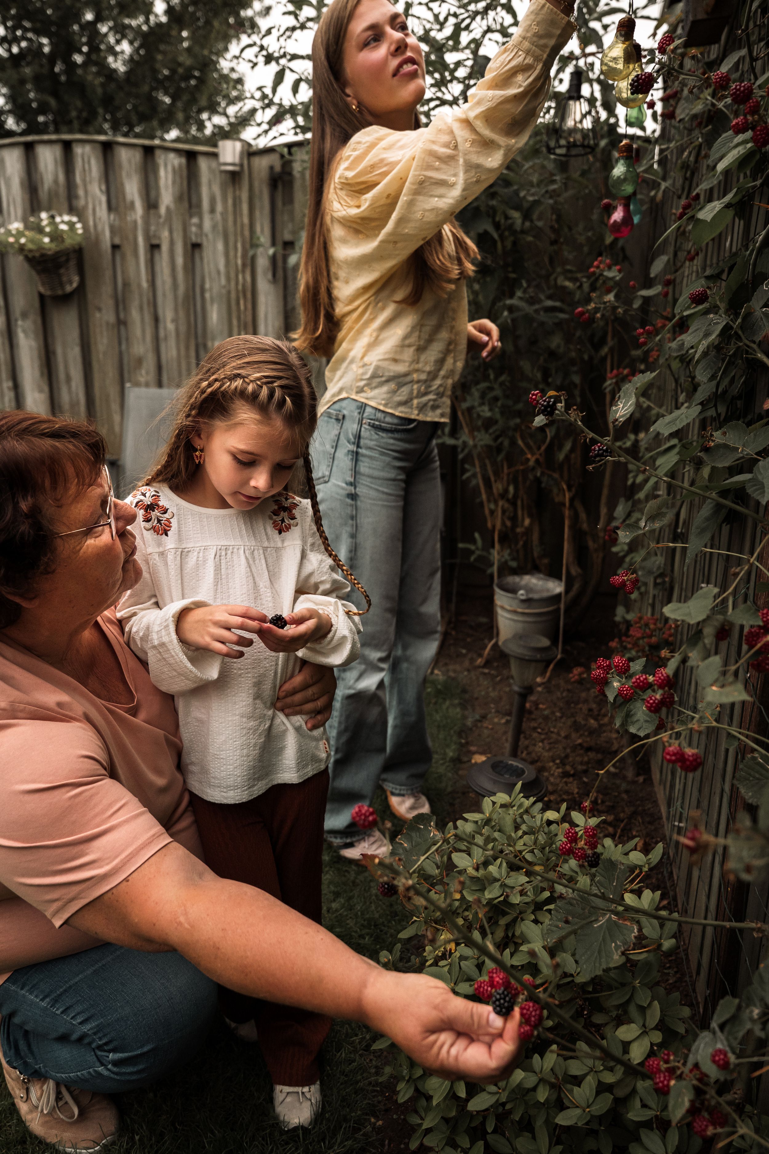 Parent and child share a tender moment exploring flowers and plants together in a backyard garden setting.