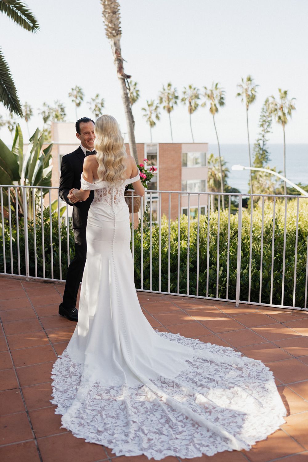 A romantic wedding couple shares intimate moments on a terrace overlooking palm trees and ocean views.