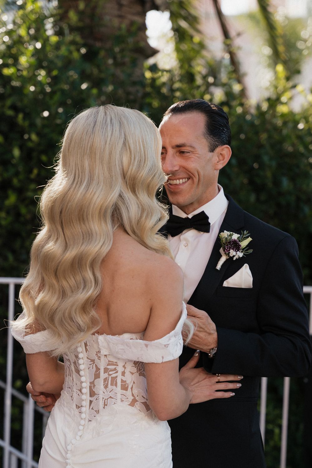 Intimate wedding moment captured outdoors with the bride's detailed lace dress and groom's classic bow tie.