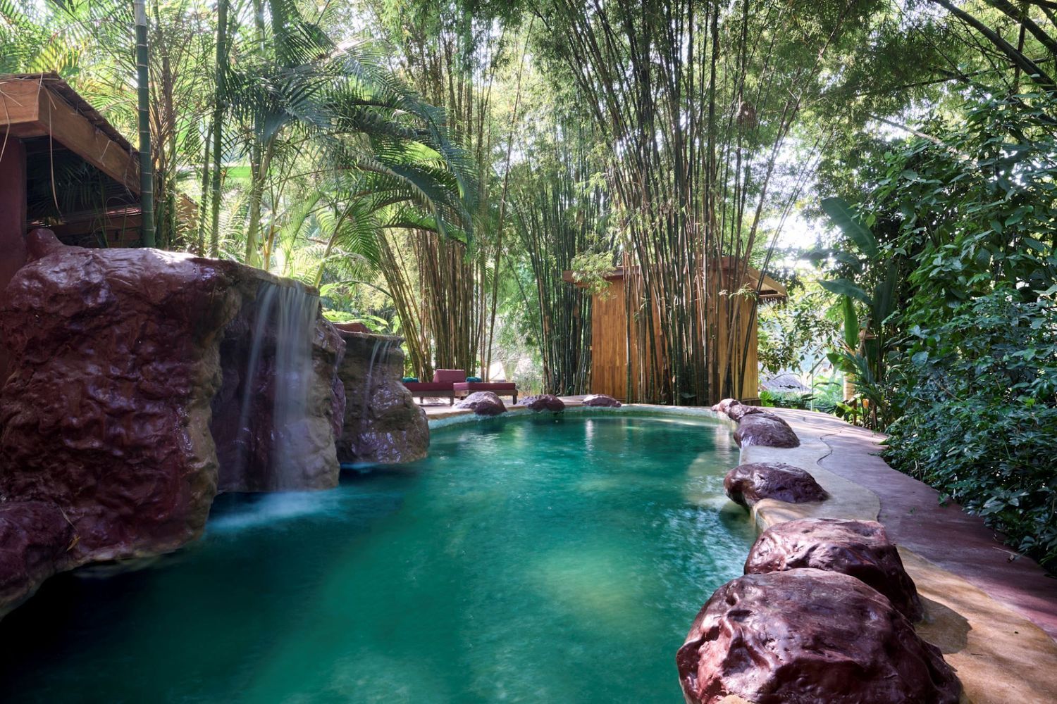 A tranquil natural swimming hole surrounded by lush tropical vegetation and rock formations in a rainforest setting.