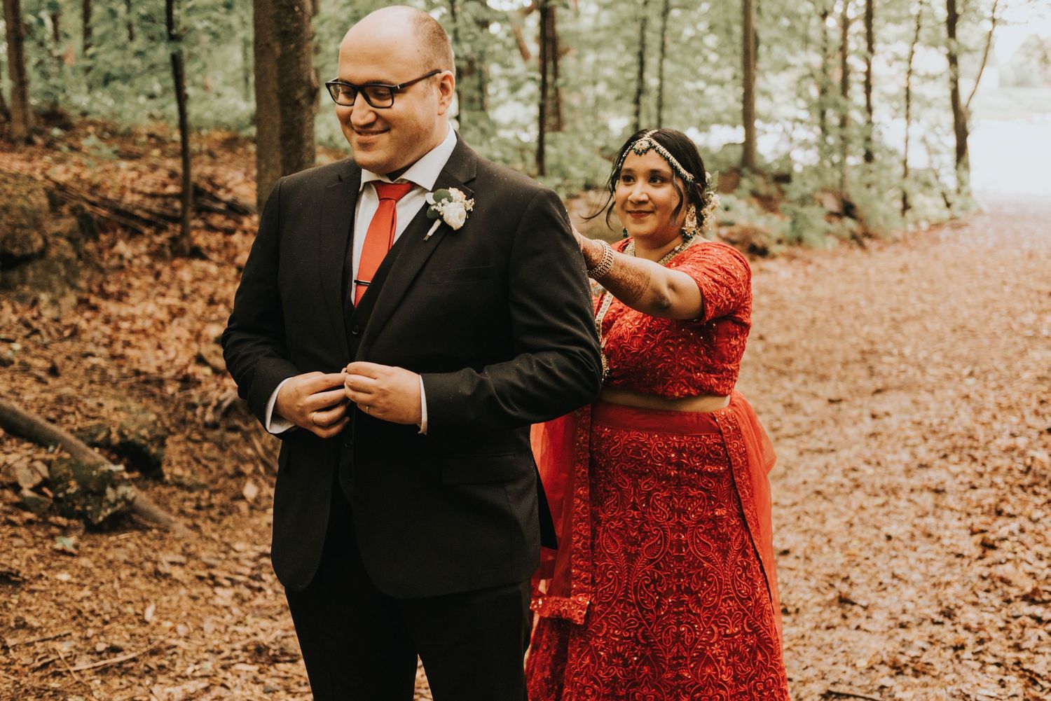 A romantic forest scene with a couple in formal attire standing among fall foliage.
