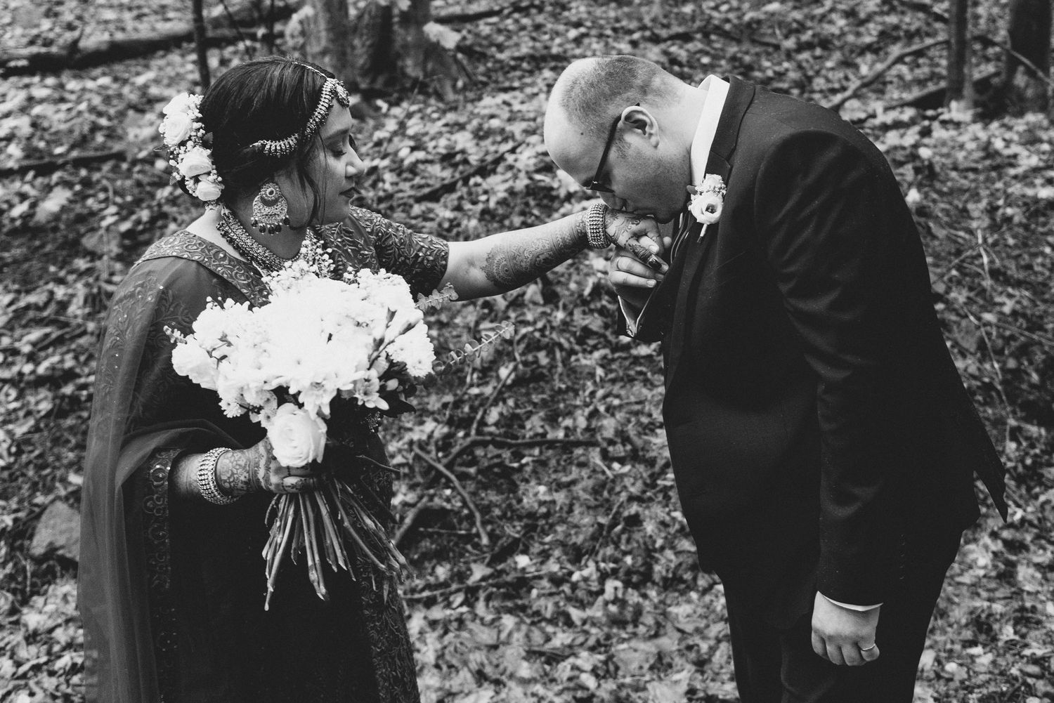 A black and white photo of a tender moment between a couple in formal attire during a wedding ceremony in the woods.