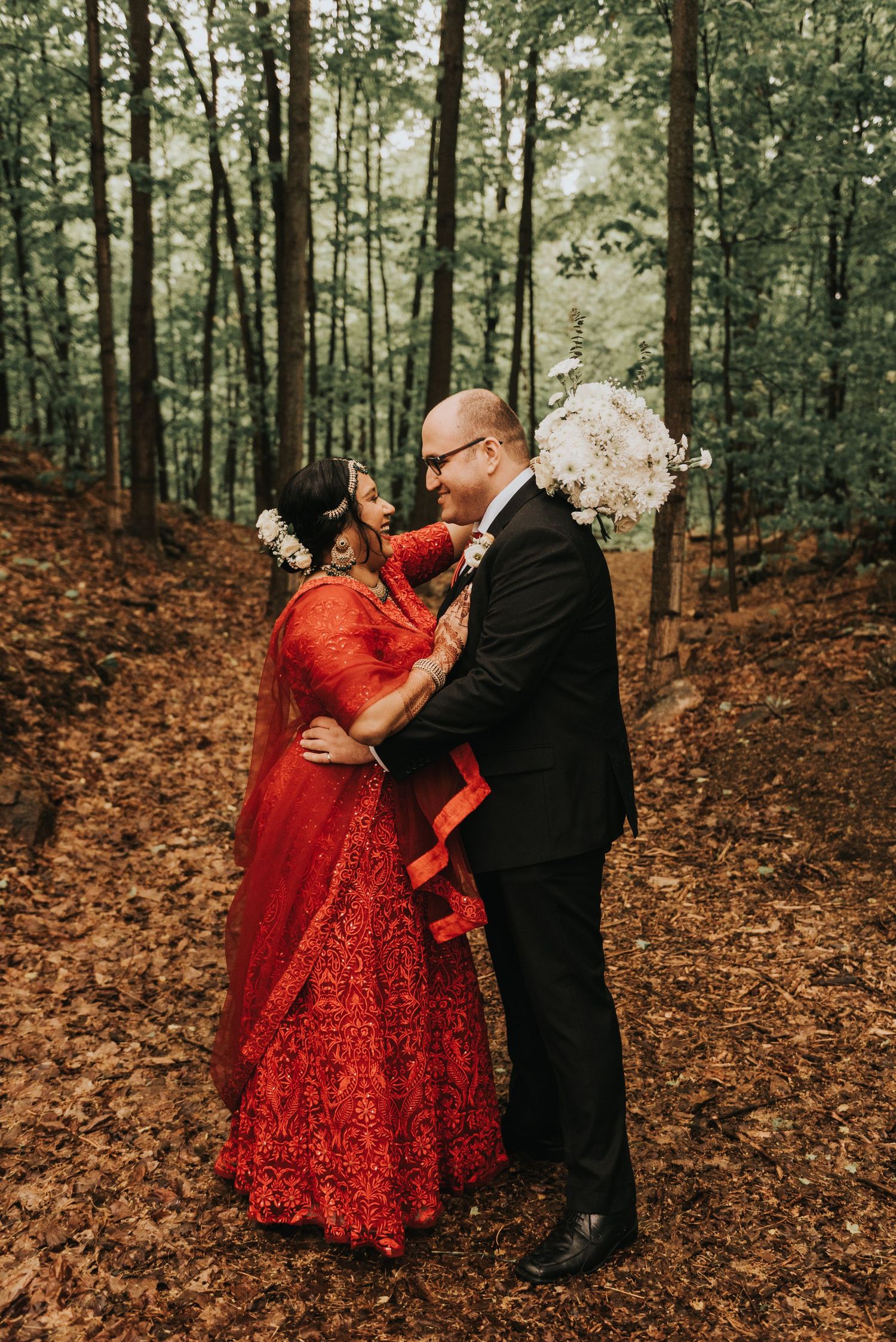 A couple shares intimate moments in a forest setting with the bride wearing a stunning red sequined dress.