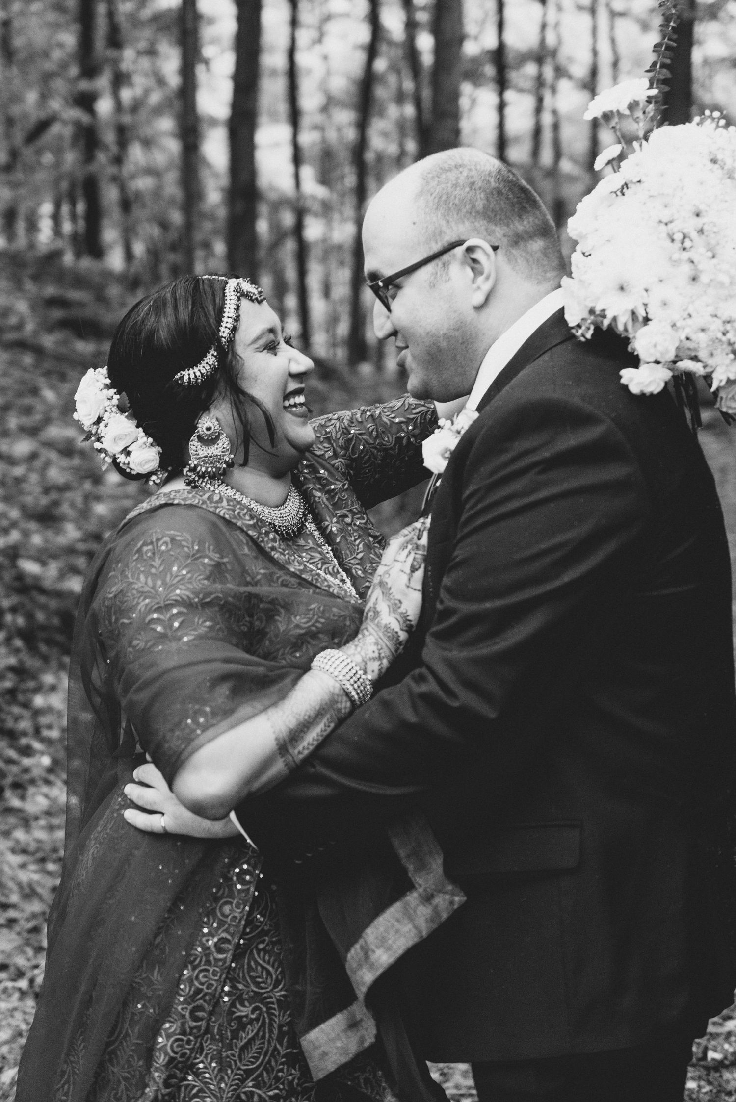 A romantic couple embraces in a forest setting wearing formal attire with black and white tones.