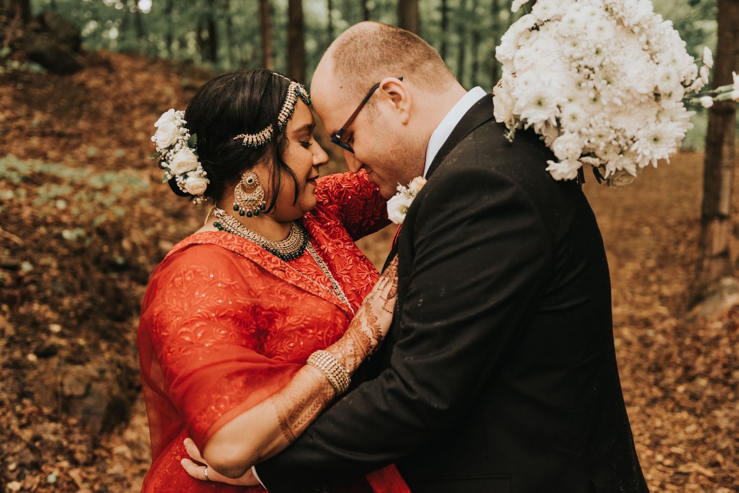 A couple shares an intimate moment outdoors wearing traditional red and black formal wear.