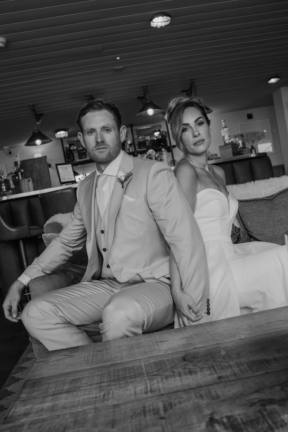 Black and white editorial portrait of a bride and groom seated back to back in the lounge at Gara Rock Hotel, captured during a modern coast
