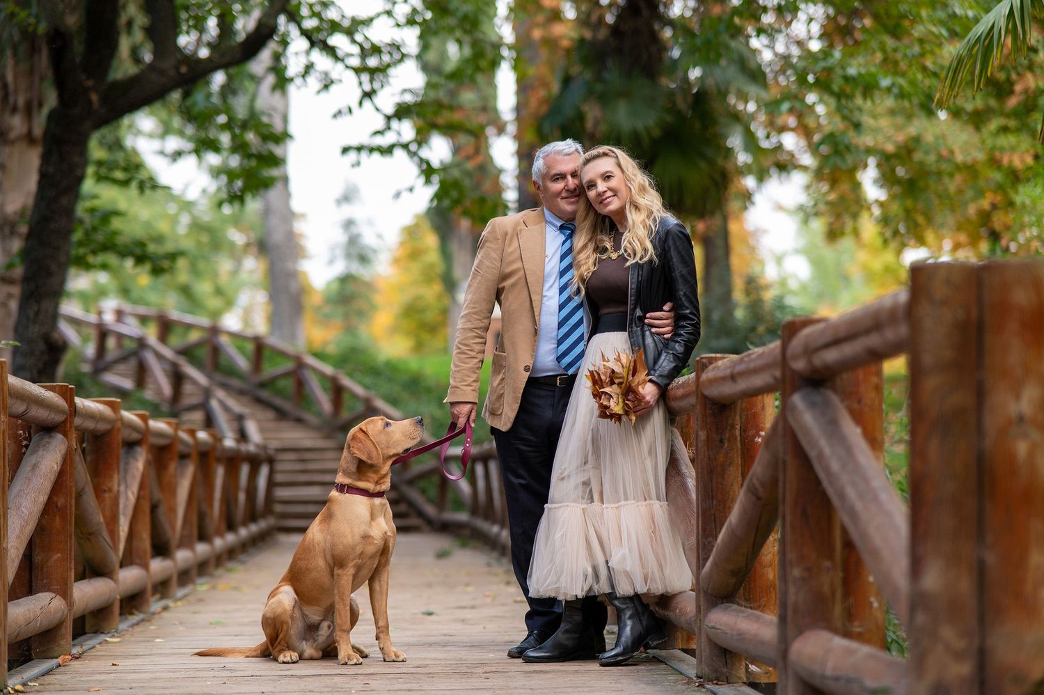 A couple poses affectionately by a scenic lake during a romantic outdoor photoshoot in a park setting.