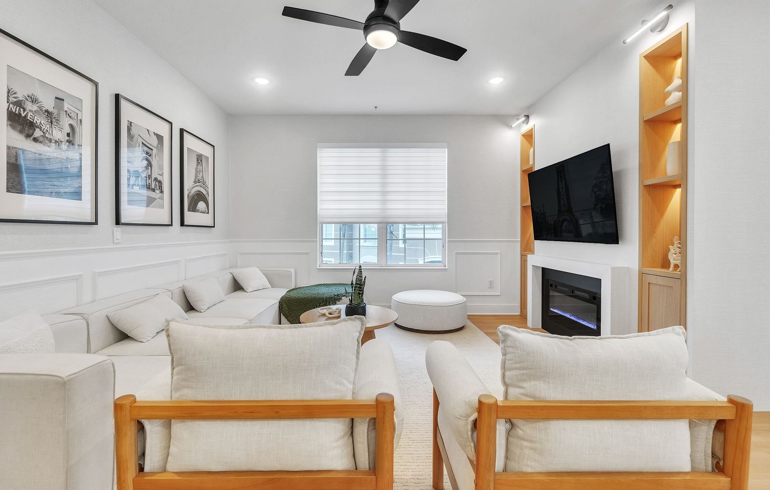 Modern white bedroom interior with wooden furniture, ceiling fan, and wall art displayed in a gallery style arrangement.