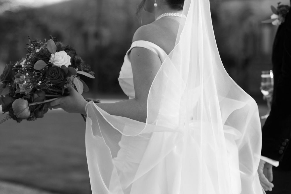A flowing white wedding veil catches sunlight while billowing in the breeze during an outdoor ceremony.