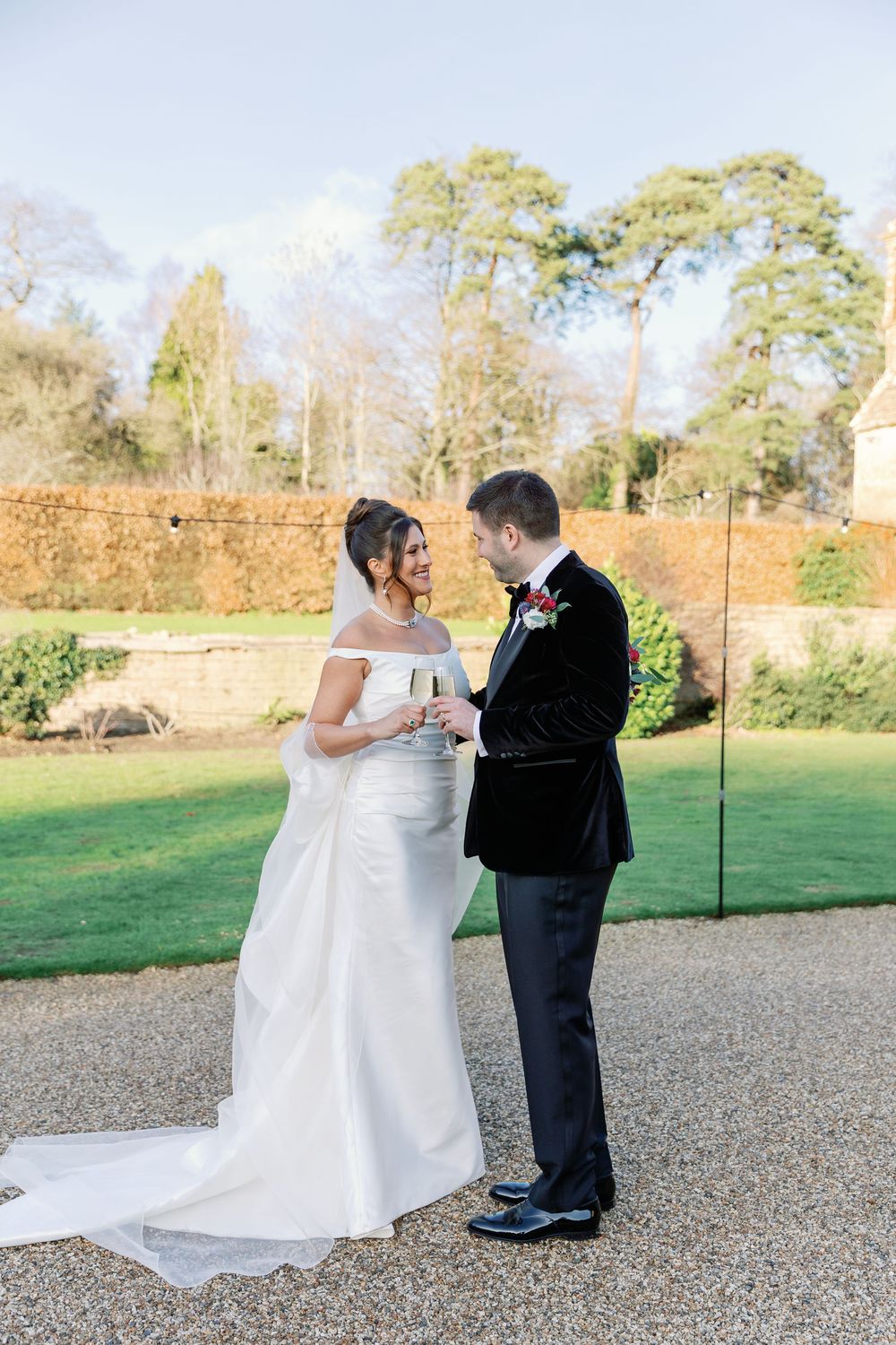 Elegant wedding couple shares intimate moment on gravel path beside stone wall at sunset.