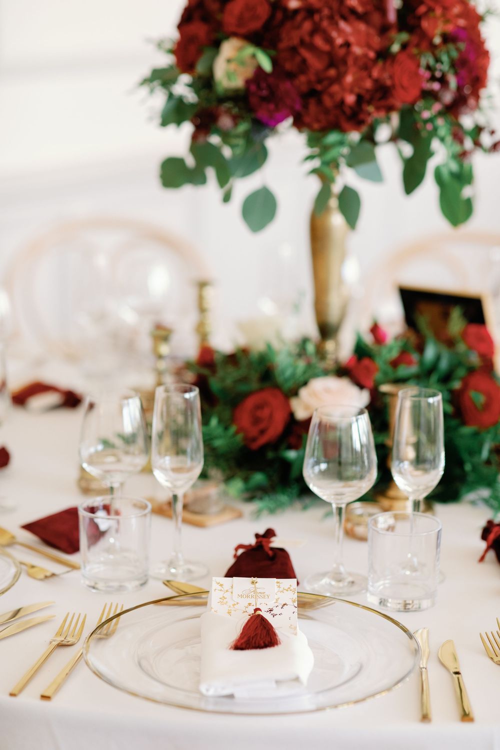 Elegant table setting with deep red floral centerpieces, gold cutlery, and crystal wine glasses.