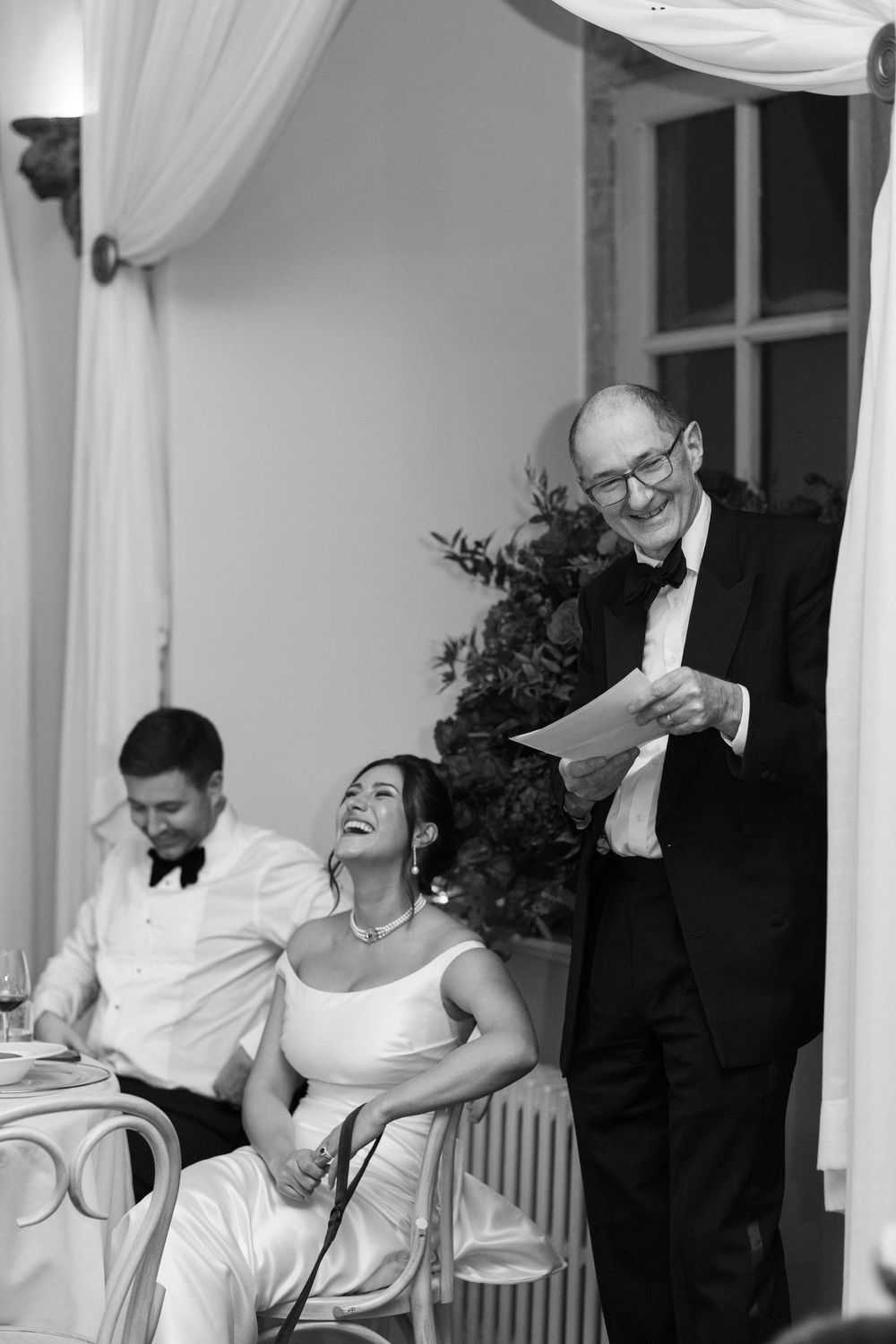 A black and white candid photo of people at a formal event sharing a joyful moment during a speech.