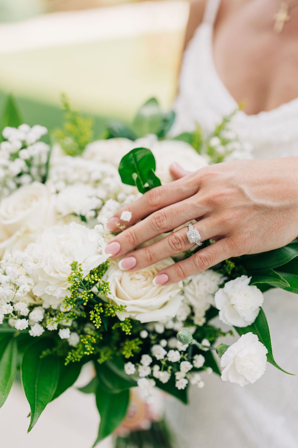 Close up of hands with engagement ring touching white and green floral wedding bouquet arrangements at The Barn South