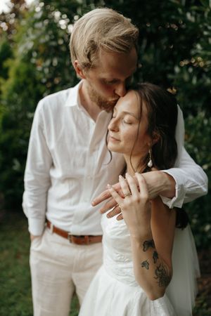 A romantic outdoor photoshoot shows a couple in white attire sharing intimate moments against a natural backdrop.