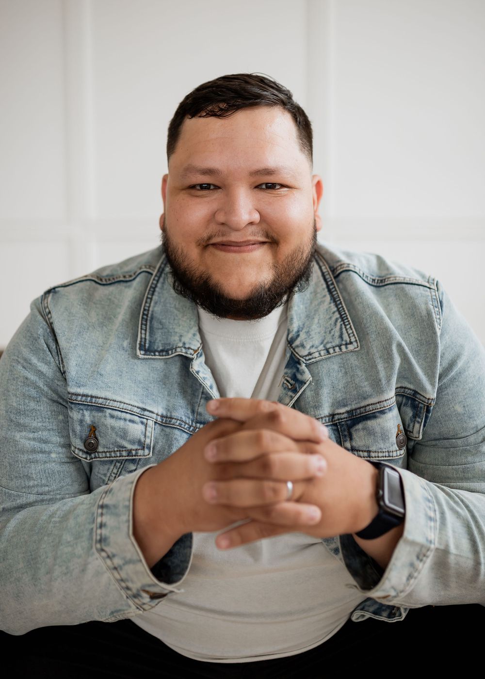 Person wearing light denim jacket and white shirt sits with clasped hands in sequence of similar poses.