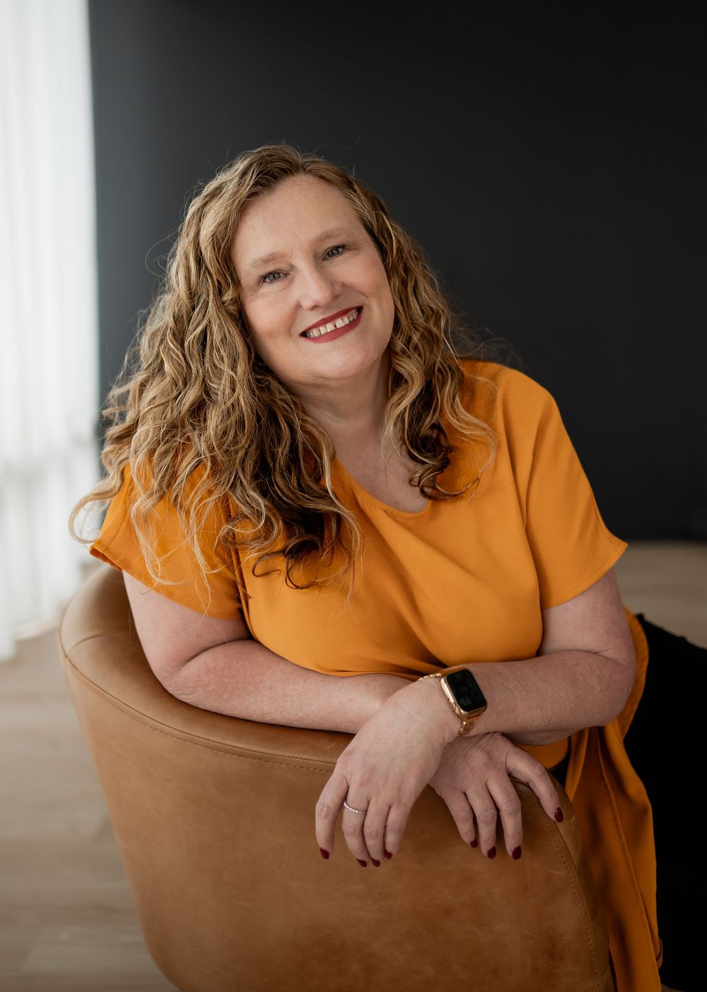 A person in an orange shirt leans comfortably on a tan leather chair in a bright, modern space.