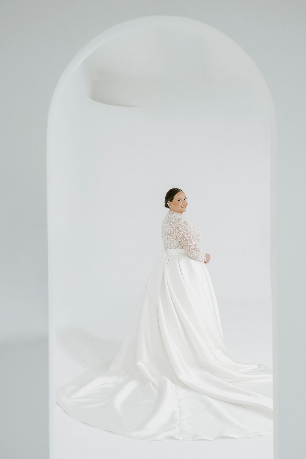 A figure draped in flowing white fabric sits against a minimalist white background in an artistic composition.
