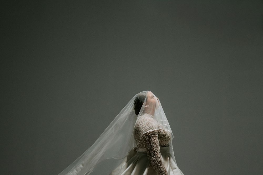 A dramatic artistic portrait in dark tones showing someone wearing a flowing veil against a moody background.