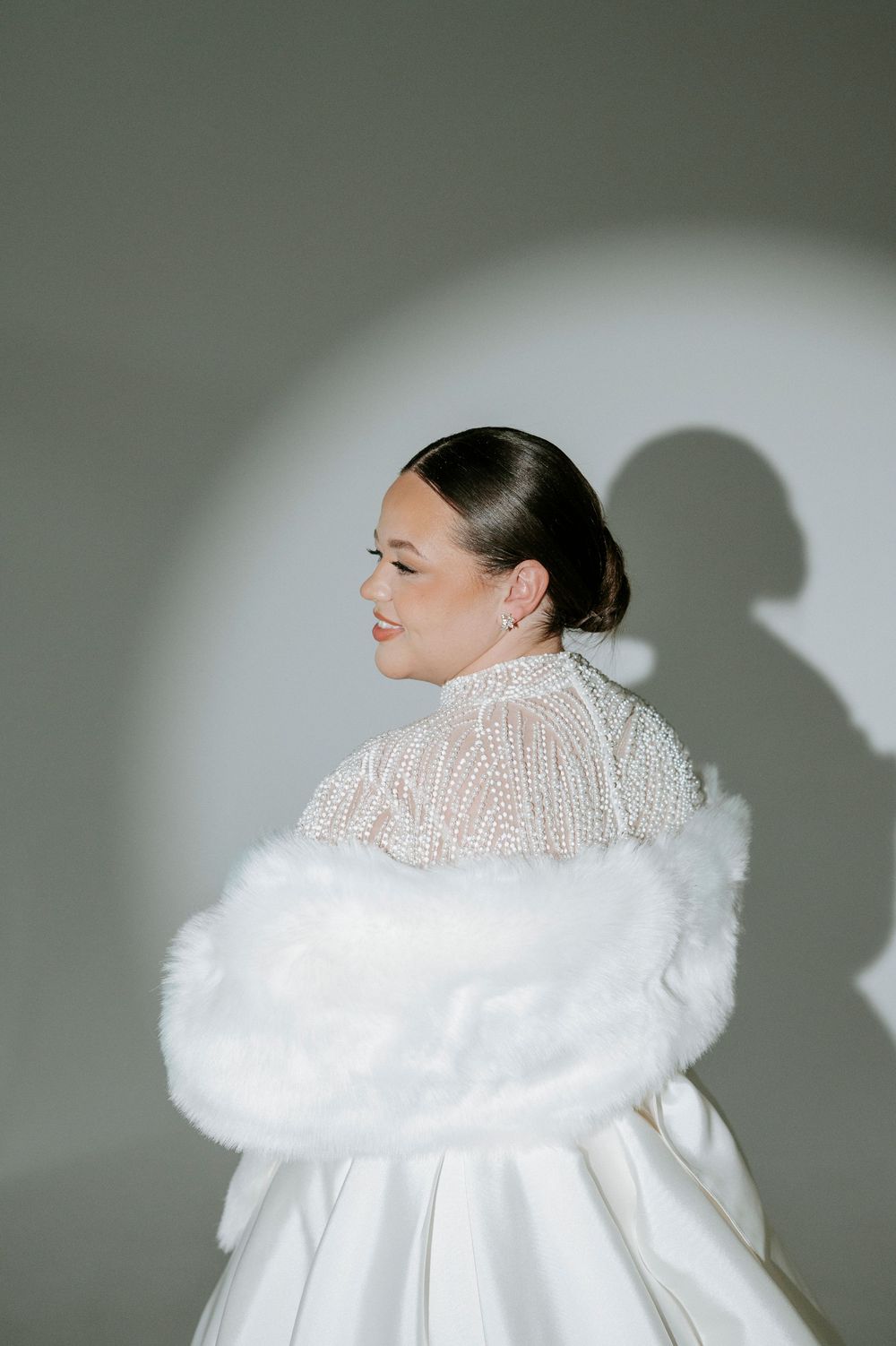 Fashion model wearing a dramatic white ruffled high-neck gown with feather trim in a minimalist studio setting.
