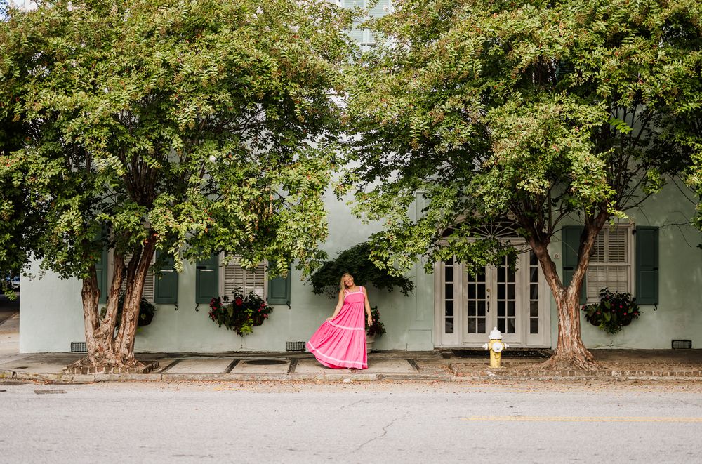 A row of rustic white buildings with green trim nestled under mature shade trees.