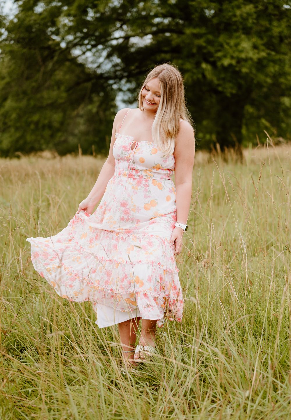 A figure in a floral summer dress twirls playfully in a sunlit meadow of tall grass.