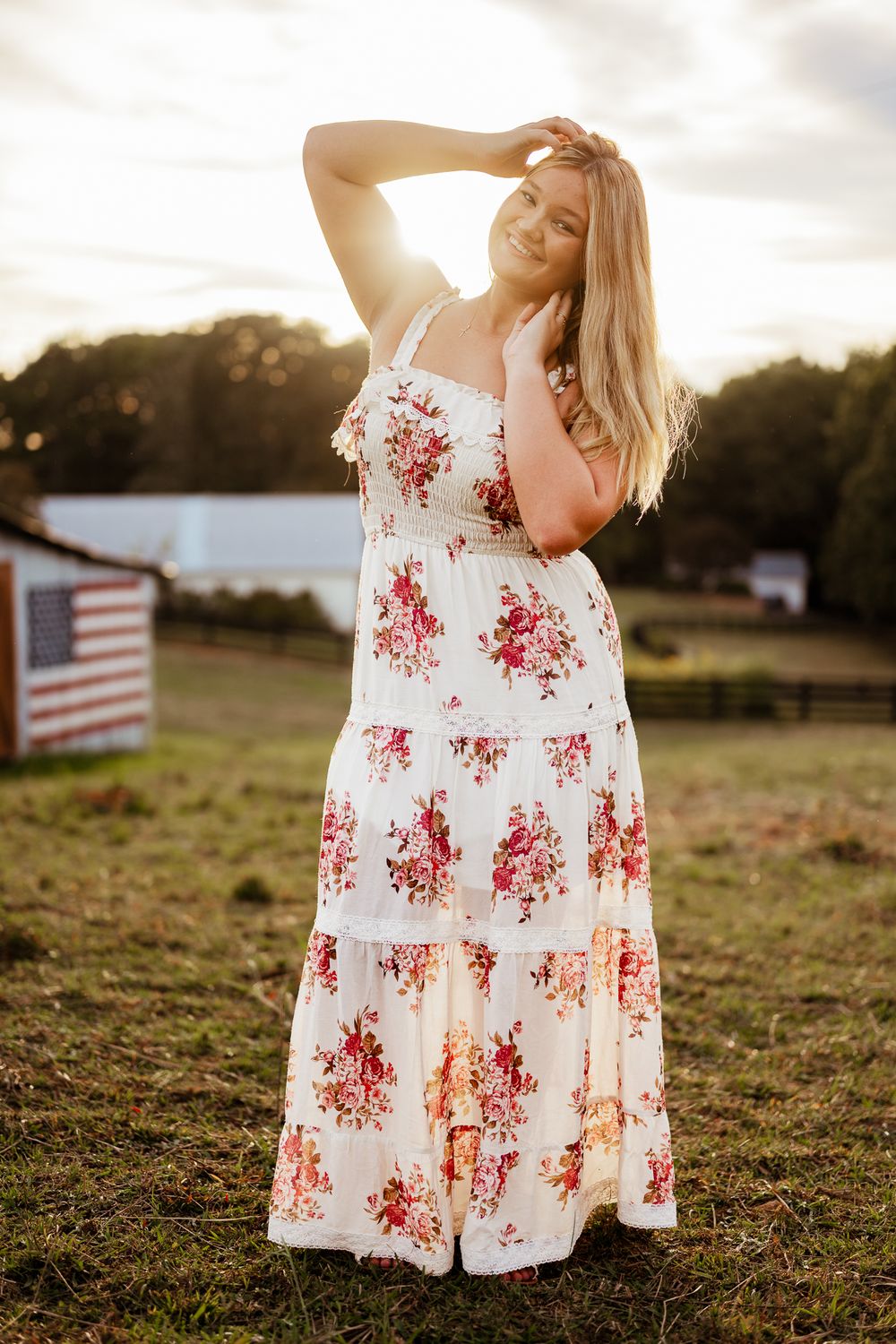 A white floral sundress with red floral pattern flows in the breeze at sunset with an American flag in the background.