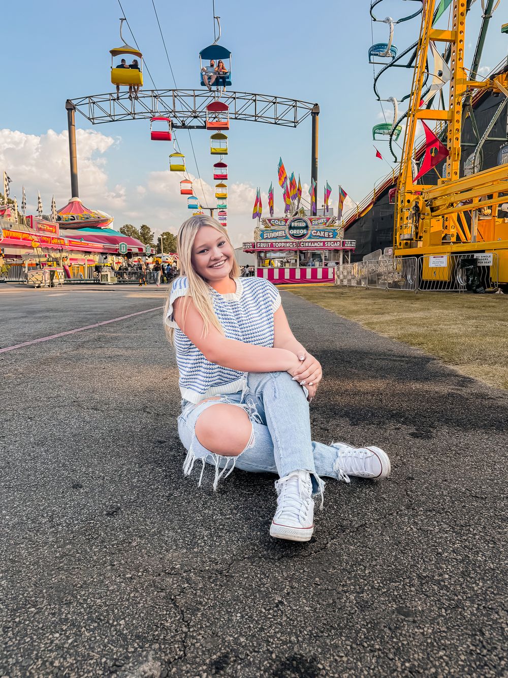A colorful carnival scene with rides, flags and string lights overhead on a summer evening at a fairground.