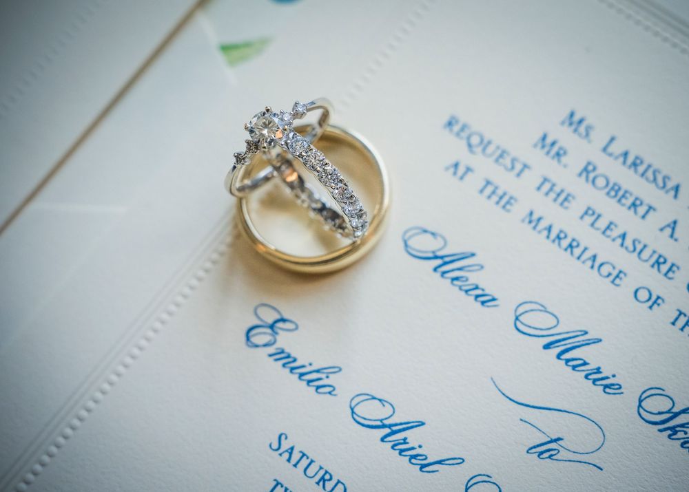 Diamond engagement ring and gold wedding band resting on elegant blue and white wedding invitation.