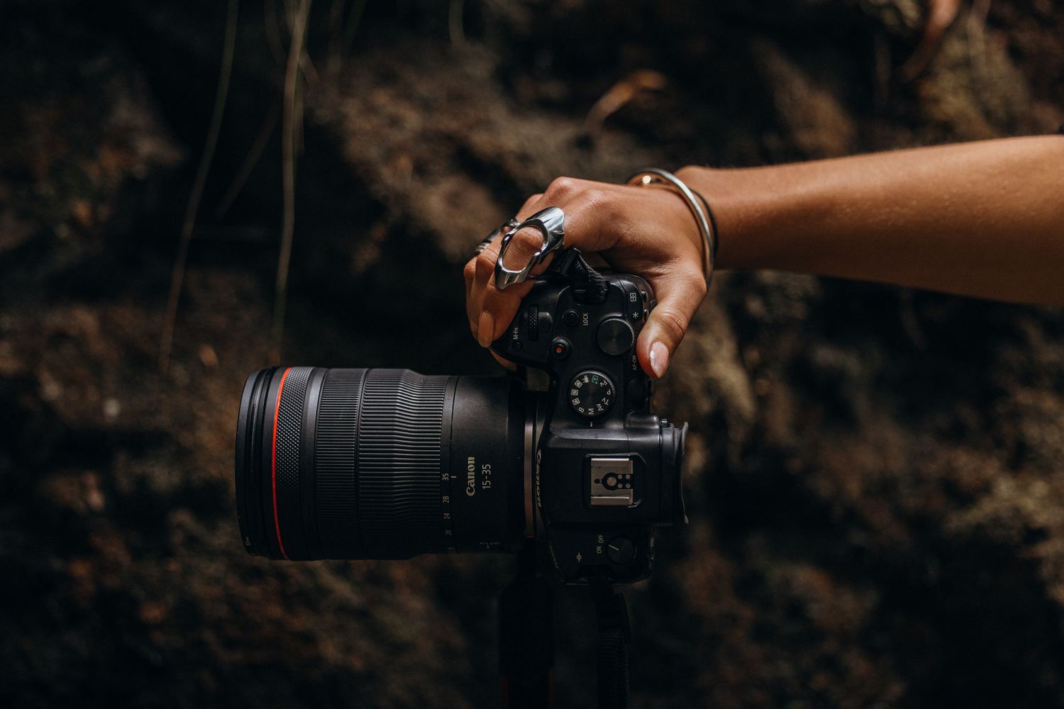 A hand holds a professional DSLR camera with telephoto lens against a dark background.