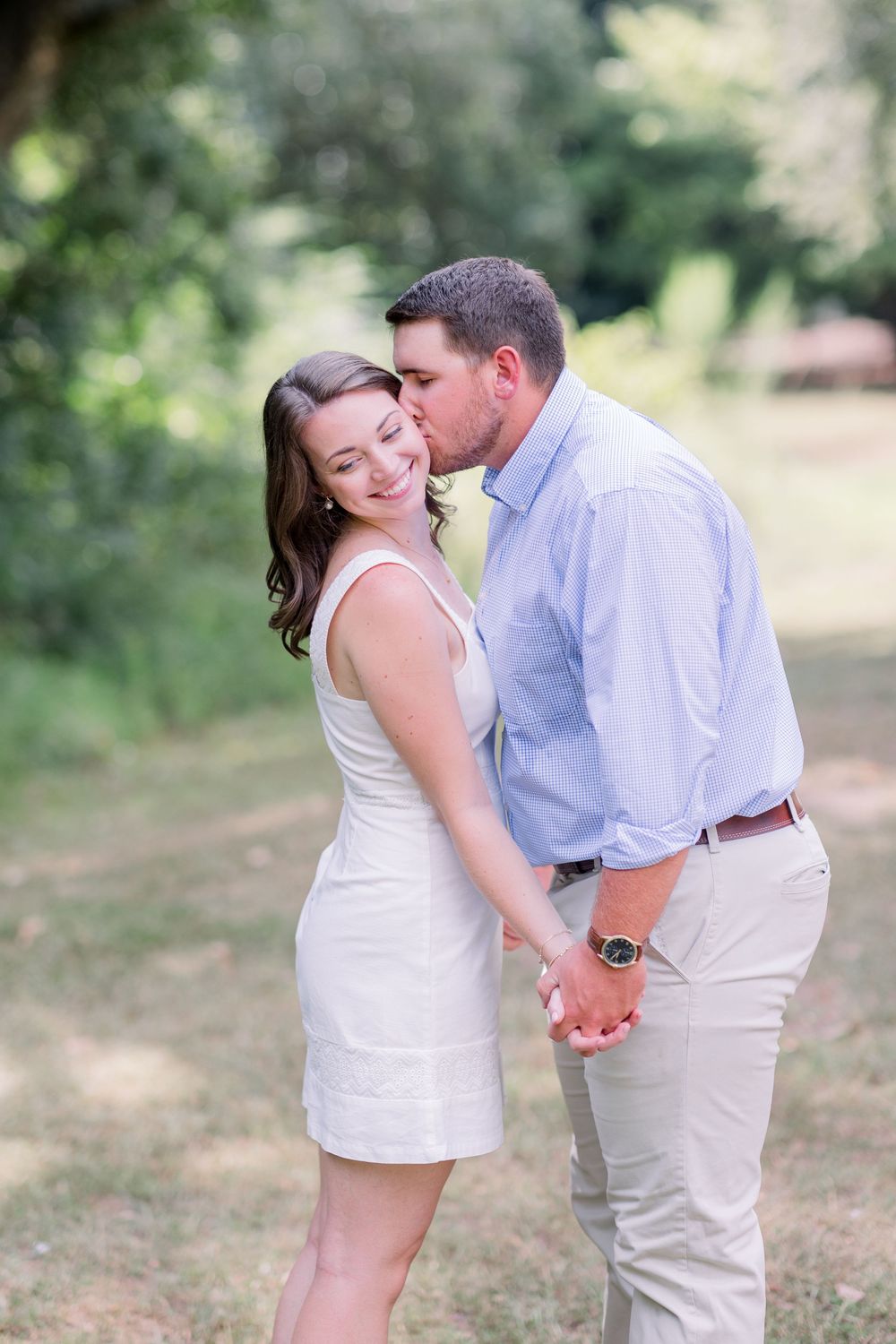 A tender embrace between a couple in light summer clothing against a natural outdoor backdrop.