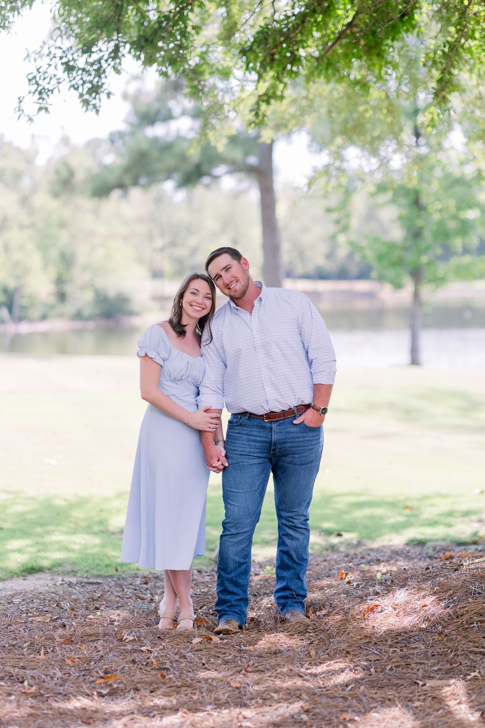 A couple shares a tender moment together under green trees in a park setting.