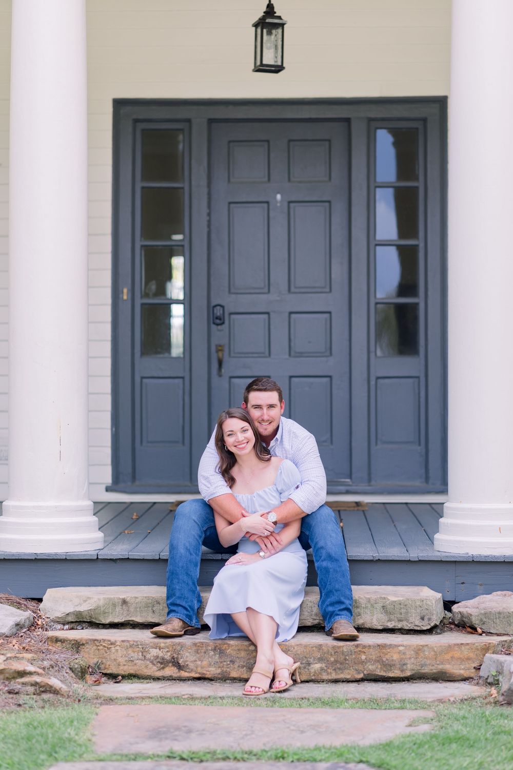 A couple sits close together on stone steps outside a building with blue doors and white columns.