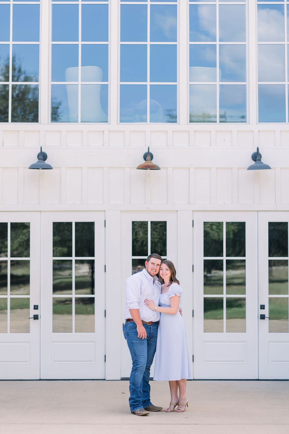 A couple stands together in front of white French doors and large windows at an elegant venue.